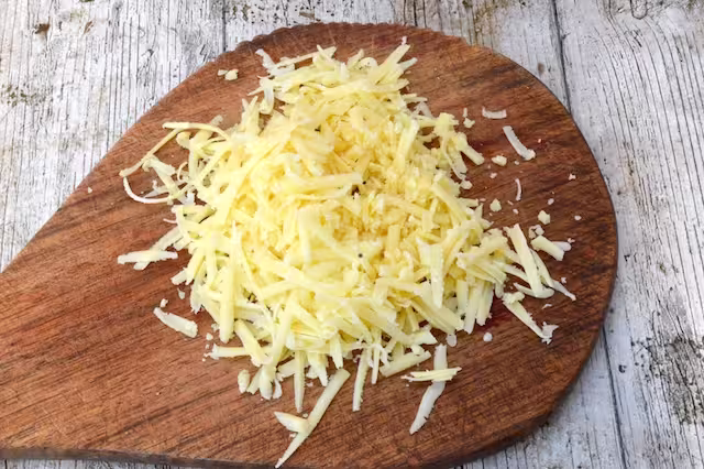 Pile of grated cheddar cheese on board.