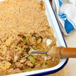 Dish of homemade cheesy leek and bean crumble with portion removed.