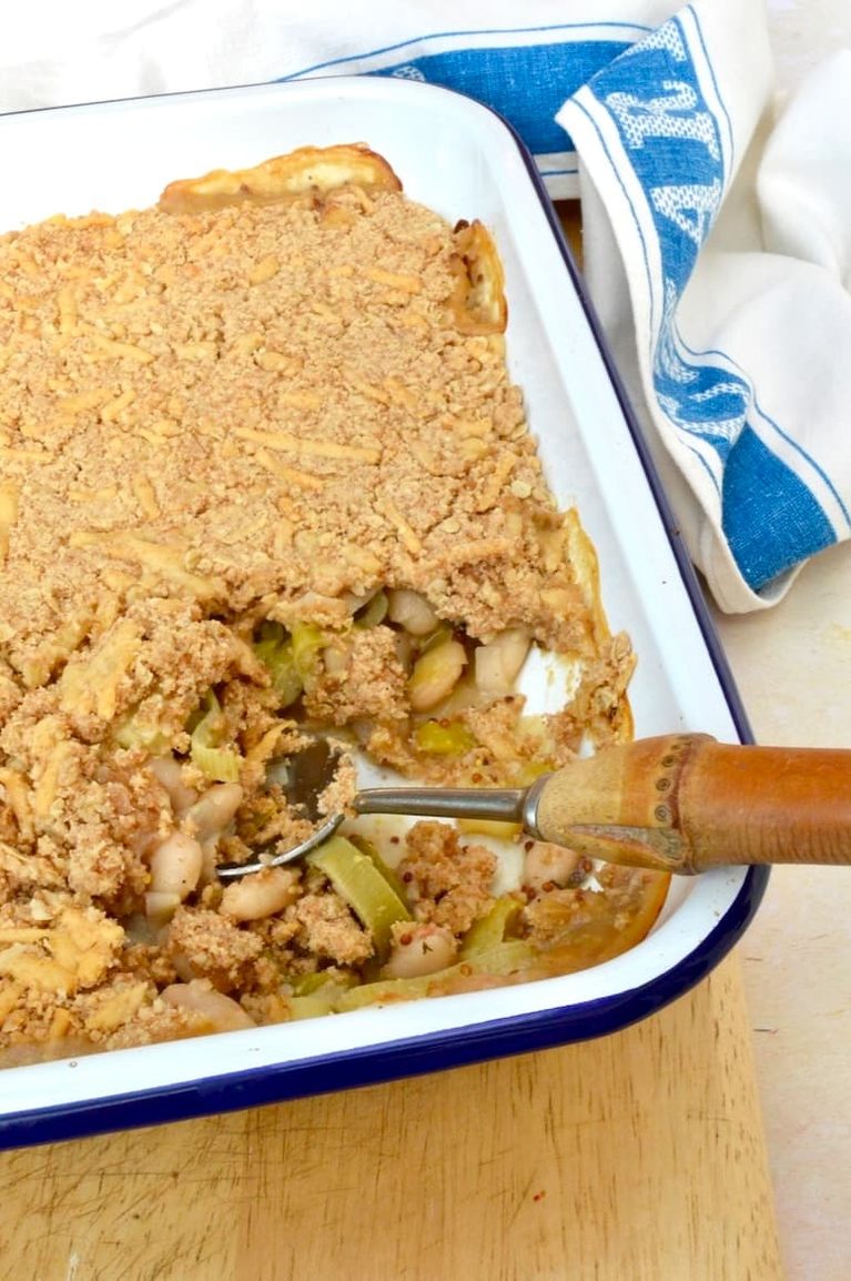 Dish of homemade cheesy leek and bean crumble with portion removed.